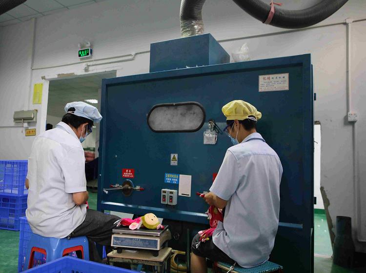 Worker filling plush toys with polyester fibre at a stuffing machine