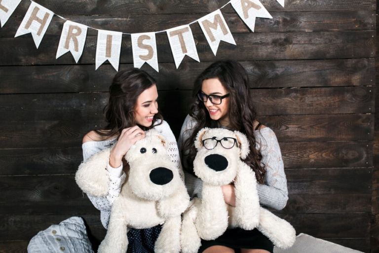 Two women hugging large white plush dog mascots at a Christmas event