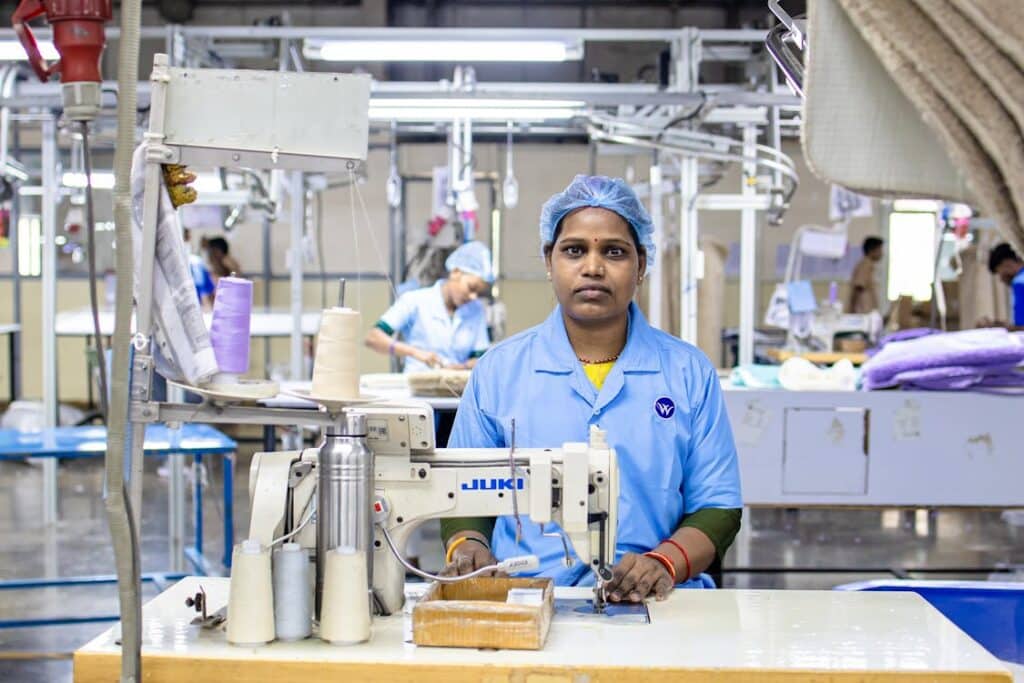 Female textile worker operating an industrial sewing machine on a factory production line, illustrating the cut-and-sew process behind plush toy manufacturing.