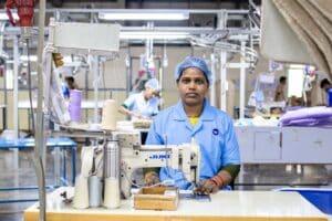 Female textile worker operating an industrial sewing machine on a factory production line, illustrating the cut-and-sew process behind plush toy manufacturing.